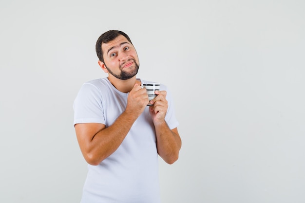 Jovem de camiseta branca segurando a xícara e parecendo satisfeito