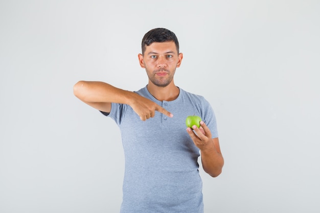 Jovem de camiseta cinza apontando o dedo para uma maçã verde