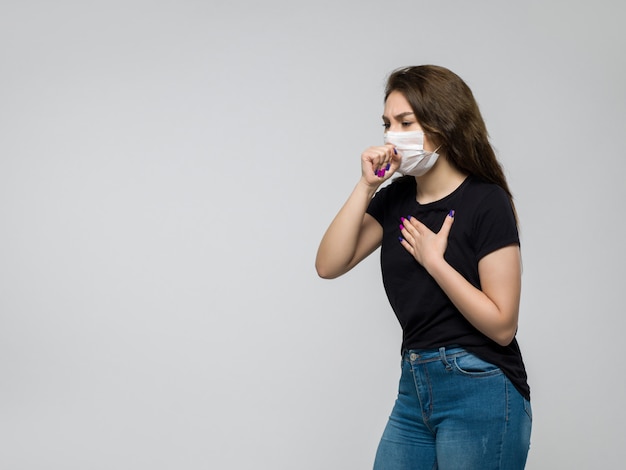 Foto grátis jovem de camiseta preta e calça jeans azul com máscara branca estéril tosse