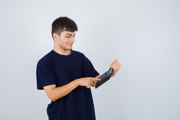 Jovem de camiseta preta fazendo cálculos na calculadora e parecendo ocupado, vista frontal.