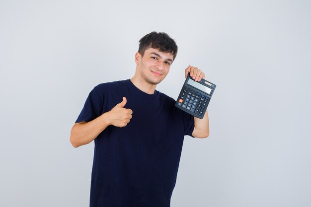 Jovem de camiseta preta segurando calculadora, aparecendo o polegar e parecendo satisfeito, vista frontal.