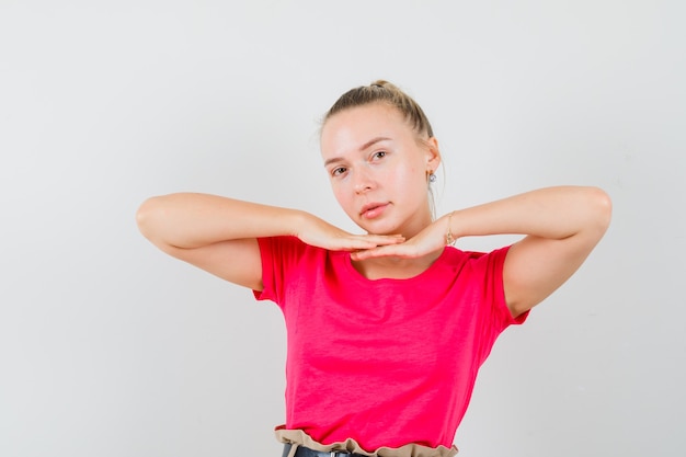 Jovem de camiseta rosa de mãos dadas embaixo do queixo e linda