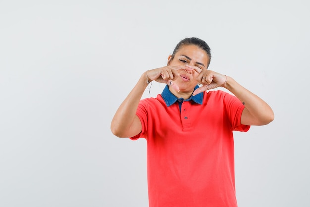 Jovem de camiseta vermelha, mostrando a forma geométrica com as mãos e olhando com foco, vista frontal.