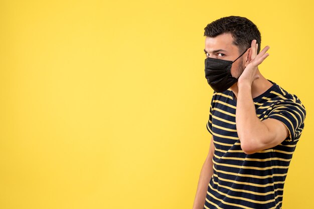 Jovem, de frente, com camiseta listrada em preto e branco, ouvindo algo amarelo.