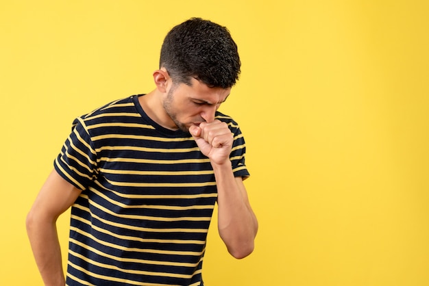 Jovem, de frente, com camiseta listrada em preto e branco, tossindo em um fundo amarelo isolado