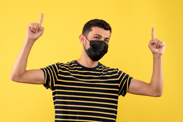 Jovem, de frente, com uma camiseta listrada em preto e branco apontando com os dedos para cima