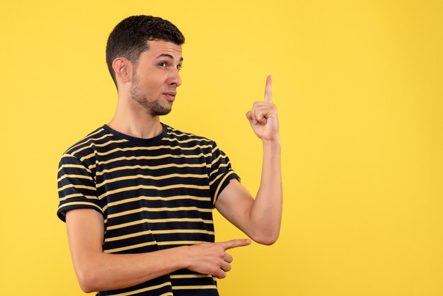 Jovem, de frente, com uma camiseta listrada em preto e branco, em pé sobre um fundo amarelo isolado