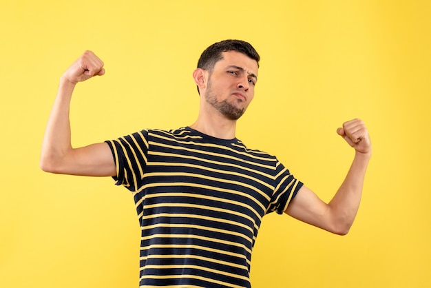 Jovem de frente para a frente com uma camiseta listrada em preto e branco fazendo um gesto vencedor em um fundo amarelo isolado