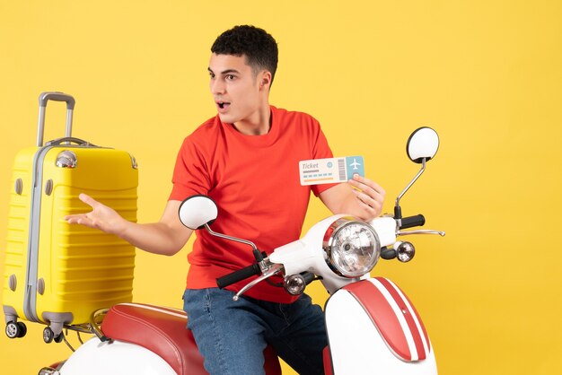 Jovem de frente para o ciclomotor com a mala amarela segurando o ingresso