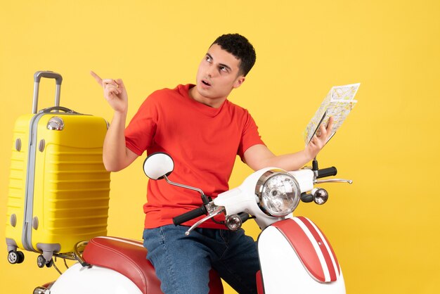 Jovem de frente para o ciclomotor segurando um mapa, olhando para algo