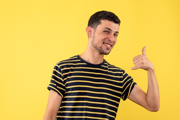 Jovem de frente para o homem com uma camiseta listrada em preto e branco fazendo sinal de me chamar sobre fundo amarelo isolado