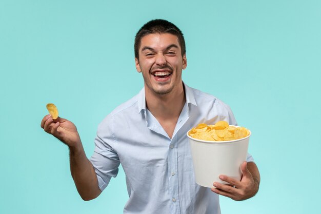 Jovem, de frente, segurando uma cesta com batatas cips e rindo no cinema remoto de filme de parede azul claro