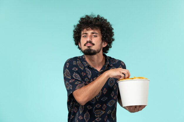 Jovem, de frente, segurando uma cesta com batatas cips na parede azul remoto filme cinema cinematográfico