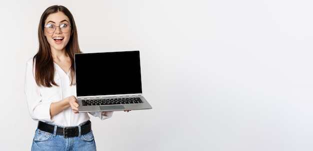 Foto grátis jovem de óculos mostrando a tela do laptop demonstrando promoção no site do computador ou loja standi