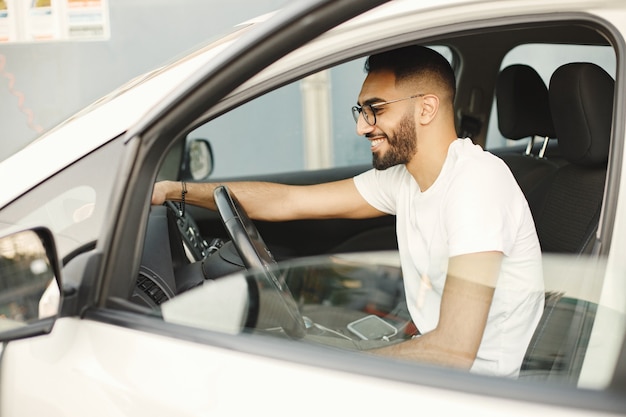 Foto grátis jovem de óculos polindo dentro de seu carro com um tapete. homem vestindo camiseta branca