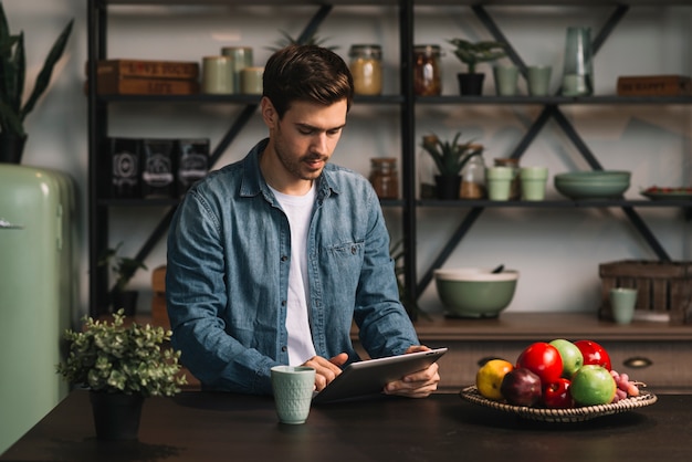 Foto grátis jovem de pé atrás da mesa olhando para tablet digital