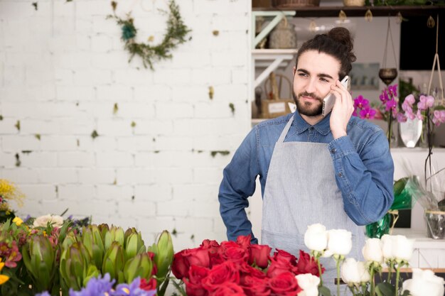 Jovem de pé atrás das belas flores falando no celular