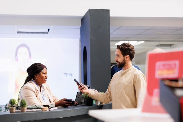 Jovem de pé no balcão de checkout de varejo segurando smartphone pagando por compras, usando tecnologia nfc para pagar roupas enquanto faz compras em loja de roupas, cliente fazendo pagamento sem contato