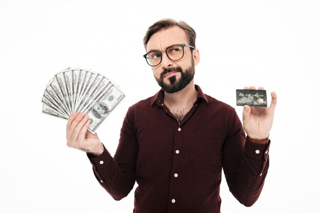 Jovem de pensamento confuso, segurando o dinheiro e cartão de crédito.