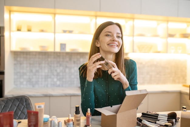 Jovem de vestido verde representando novos cosméticos e parecendo contente