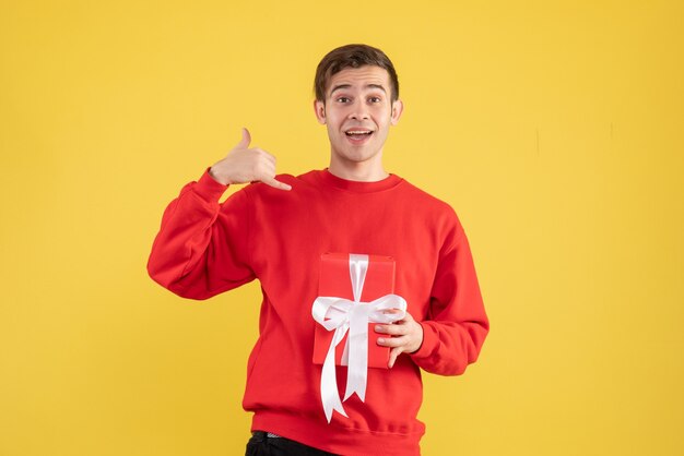 Jovem de vista frontal com suéter vermelho, fazendo sinal de chamada em fundo amarelo