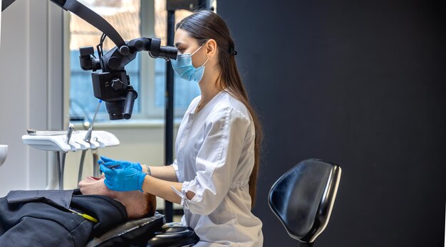 Jovem dentista tratando dentes de pacientes com microscópio dental conceito de odontologia