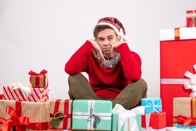 Jovem deprimido sentado em frente aos presentes de Natal