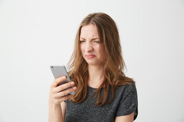 Foto grátis jovem descontente descontente, olhando para a tela do telefone.