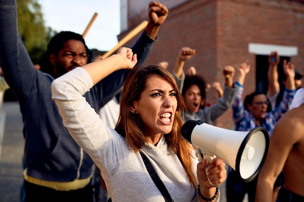 Jovem descontente usando megafone e gritando enquanto protestava com grupo de pessoas nas ruas da cidade