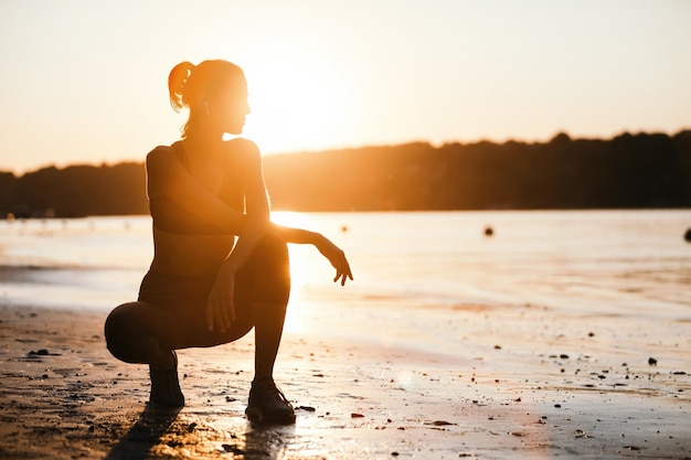 Jovem desportista agachada à beira do rio e aproveitando o sol da manhã Copiar espaço