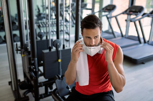 Jovem desportista colocando máscara facial protetora durante o exercício em uma academia