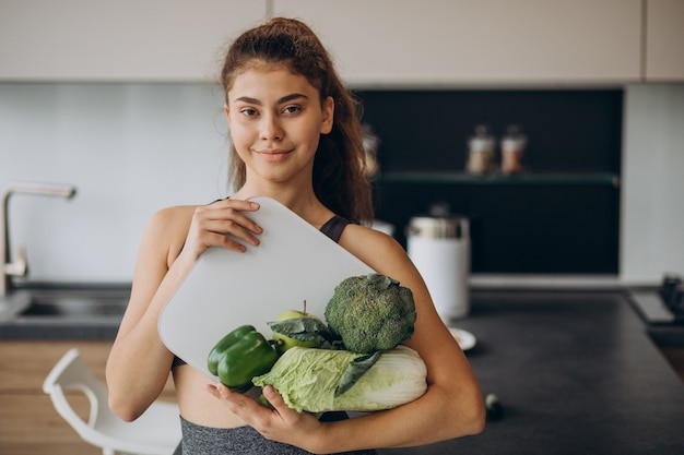 Jovem desportiva com balança e legumes na cozinha