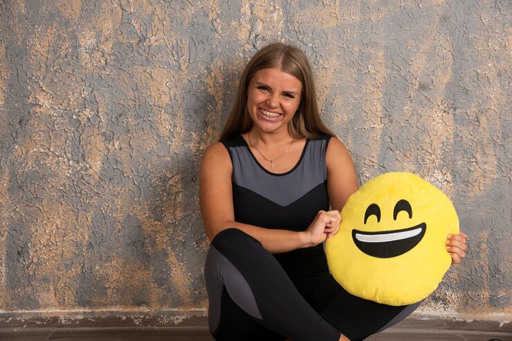Foto grátis jovem desportiva em trajes desportivos, segurando uma sorridente almofada de emoji abaixo.