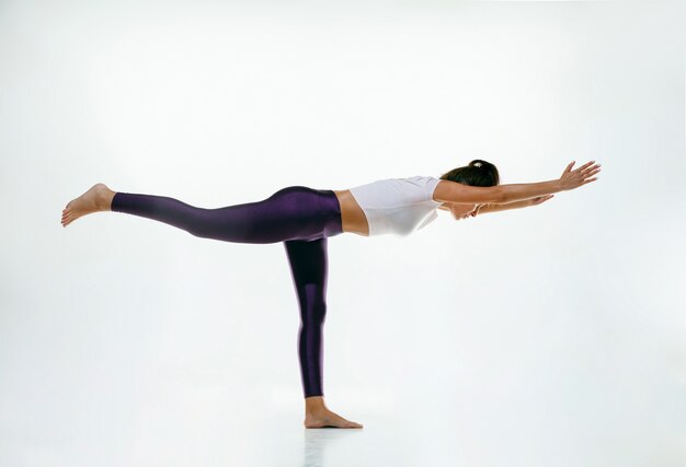 Jovem desportiva fazendo prática de ioga isolada no espaço em branco. Modelo feminino flexível apto praticando