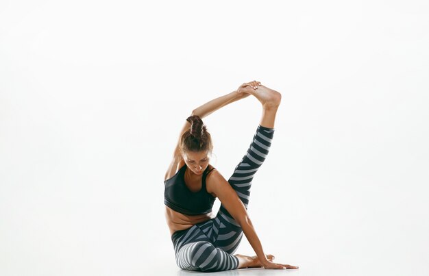 Jovem desportiva fazendo prática de ioga isolada no espaço em branco. modelo feminino flexível apto praticando