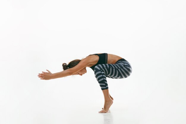 Jovem desportiva fazendo prática de ioga isolada no fundo branco do estúdio. Ajuste o modelo feminino flexível praticando. Conceito de estilo de vida saudável e equilíbrio natural entre o desenvolvimento corporal e mental.