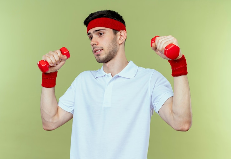 Foto grátis jovem desportivo com uma faixa na cabeça a fazer exercício com halteres, parecendo confiante sobre o verde
