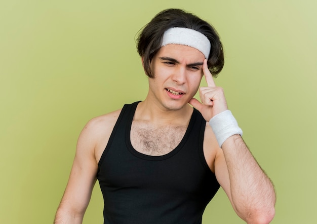 Jovem desportivo vestindo roupas esportivas e bandana apontando para a têmpora, parecendo insatisfeito, concentrado em uma tarefa difícil