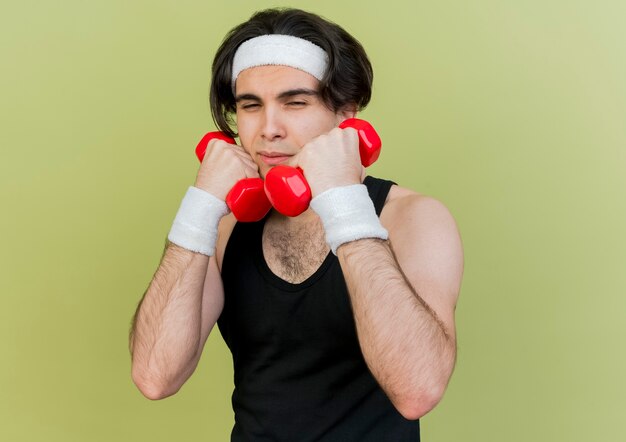 Jovem desportivo vestindo roupas esportivas e bandana, malhando com halteres sorrindo