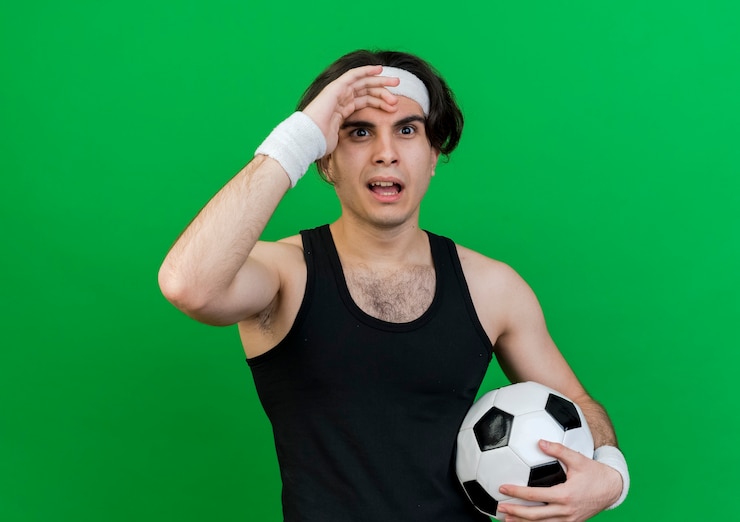 Foto grátis jovem desportivo vestindo roupas esportivas e bandana segurando uma bola de futebol sendo confundido com mão na cabeça