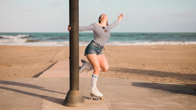 Foto grátis jovem despreocupada segurando pilar em pé na frente da praia