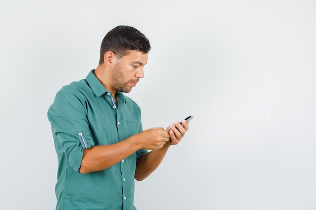 Jovem digitando em smartphone com camisa e parecendo ocupado.