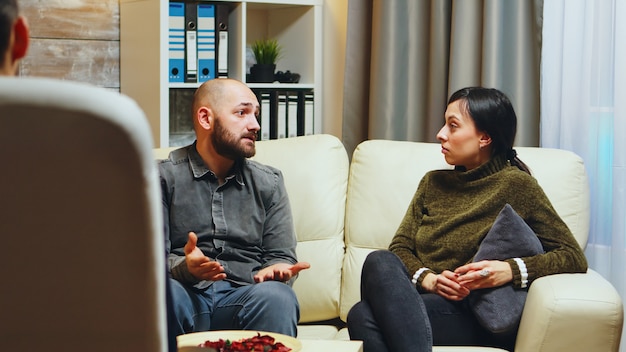 Jovem dizendo à esposa na frente do terapeuta o que o torna infeliz em relação ao relacionamento deles.