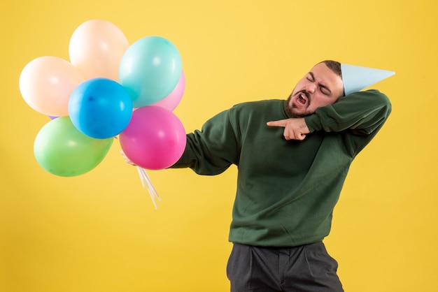 Jovem do sexo masculino com balões coloridos em fundo amarelo