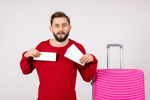 Jovem do sexo masculino com bolsa rosa segurando bilhetes em uma parede branca voo colorido viagem viagem turística de férias