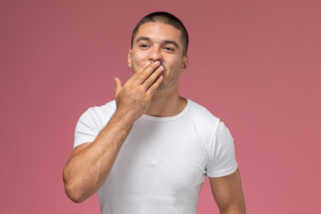 Jovem do sexo masculino com camiseta branca posando cobrindo a boca na mesa rosa