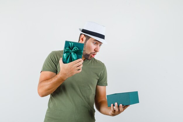 Jovem do sexo masculino com camiseta e chapéu verdes olhando para a caixa de presentes e parecendo surpreso
