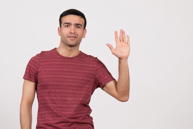 Jovem do sexo masculino com camiseta vermelha escura em pé e mostrando a palma da mão no fundo branco de frente