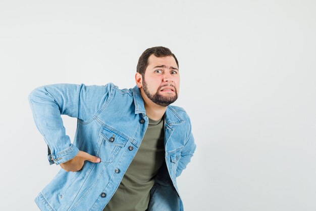 Jovem do sexo masculino com dor nas costas, vestindo uma jaqueta de camiseta e parecendo cansado