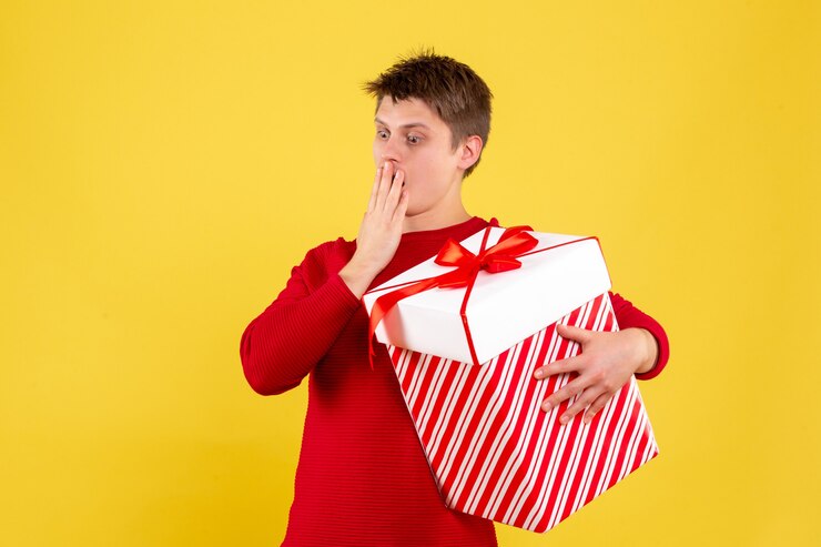 Foto grátis jovem do sexo masculino com grande natal presente em fundo amarelo